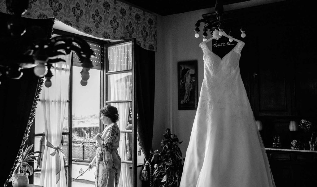 Vestido de novia colgado en una lampara, mientras que la novia habla con sus damas de honor. 
